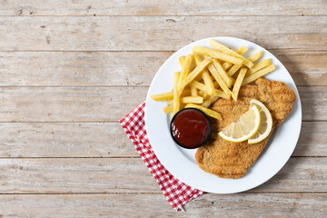Wiener schnitzel with fried potatoes on wooden table. Top view. Copy space