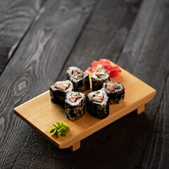 Set of california sushi rolls with eel, cucumber, wasabi and ginger in black sesame. Japanese food. Low calorie food. Dark gray wooden background. Side view. Soft focus. Copy space. 