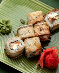 Set of sushi rolls with salmon, eel, cream cheese and cucumber. Rolls on green plate with wasabi and pickled ginger. Seafood dishes. Japanese food. Top view. Close-up. Soft focus.