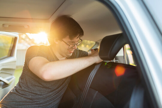 Man in car putting seat covers on back seat while listing to podcast with earbuds