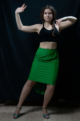 Fototapeta na wymiar Woman in black top and green skirt posing on black background