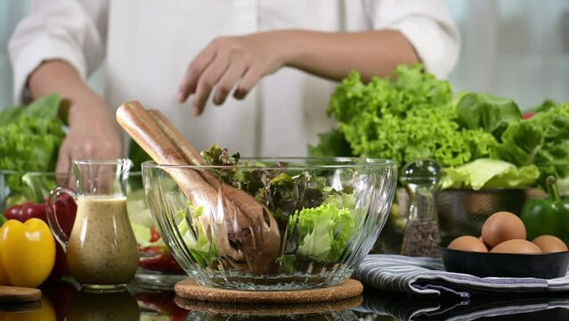 woman chef mix fresh baby cos salad and pour salad dressing in glass blow. Organic Vegetables mix all green salad In glass bowl. Breakfast fresh salad and clean vegetable.