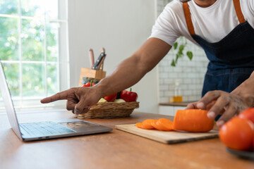 Asian strong man Wearing an apron having fun while preparing ingredients such as fruits and vegetables. learn how to do Chopping Carrots via Application Happily online in the kitchen.