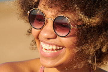 Cheerful girl with braces in fashionable sunglasses. Close-up of laughing girl with dyed frizzy hair with braces wearing stylish round sunglasses on sunny day outdoors.