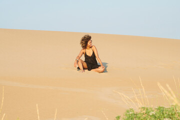 Happy woman in black dress with bare shoulders enjoying summer day on sandy dune. Relaxed woman...