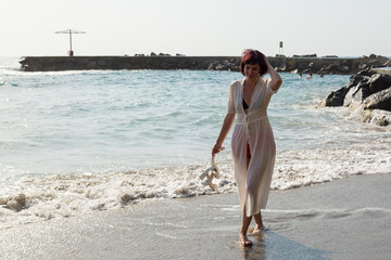Woman walking barefoot on sand and sea waves.
