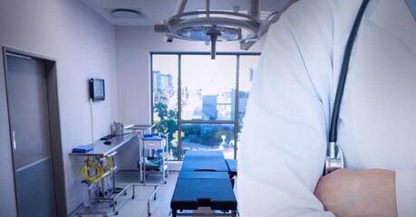Mid section of male doctor with arms crossed against operation theatre in background