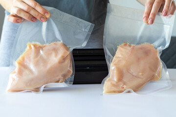 Vacuumed chicken fillet sous vide in front of a packaging machine in a woman's hands.
