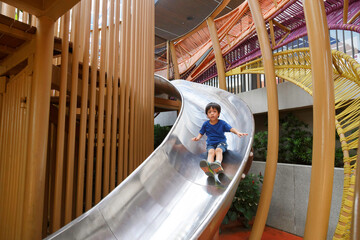 happy asian boy on playground. Kid slide down on slider at plublic playground.
