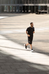 Fototapeta na wymiar Handsome strong sportsman running at the street outdoors and looking aside 