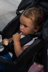 Kleinkind im Kinderwagen nachdenklich und skeptisch mit etwas zu essen in der rechten Hand