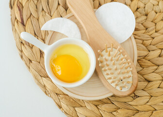 Small white bowl with raw egg and wooden hairbrush. Natural skin and hair care, homemade spa and beauty treatment recipe. Zero waste concept. Top view.