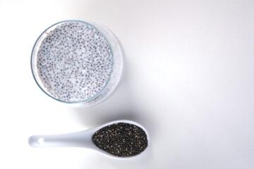 Milk pudding with chia seeds and a ceramic spoon with dry chia seeds on white background.