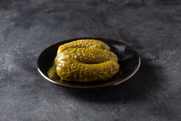 There are three pickled cucumbers on the table in a plate. On a black background.