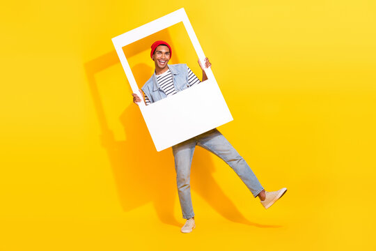 Full length photo of excited funky guy dressed denim clothes holding photo frame isolated yellow color background