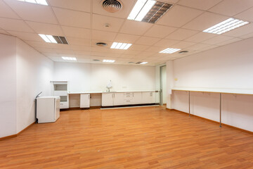 Old empty room with white kitchen furniture and sink that used to serve as office canteen for employees. A spacious and bright room, equipped as corporate dining room, needs new and fresh renovation.