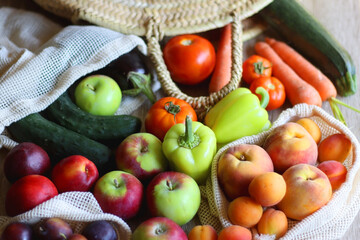 Straw bag and reusable fabric bags filled with various healthy fruit and vegetables. Wooden background, selective focus.