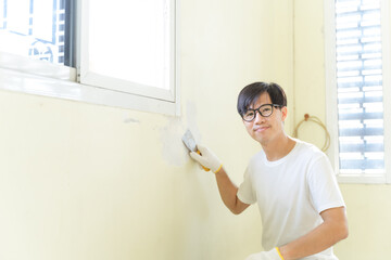 Asian painter man using scraper or spatula to remove old paint wall for cleaning, repair, preparing concrete wall before painting wall at home. Scraping to remove paint plaster peel. Painting concept.