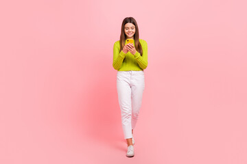 Full length photo of cute young girl walking reading news hold device wear trendy green outfit isolated on pink color background