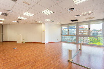 Empty office and fluorescent lamps on the ceiling in need of repair and replacement. Bright office space for rent. Light brown parquet and large panoramic windows in an empty abandoned office.