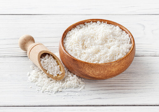 Coconut flakes in wooden bowl with scoop on white wooden background