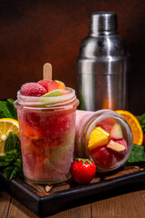 Frozen mocktail, popsicle punch with fruit and berry. Iced summer sangria with strawberry, orange, apple and fruit juice, with ingredients on wooden kitchen table background 
