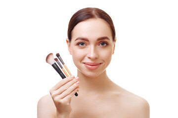 Portrait of a young brunette woman with shoulders and well-groomed skin holding cosmetic brushes near her face on a white background. The concept of make-up, cosmetic procedures, search.