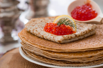 Russian traditions. Russian holiday Maslenitsa. Still life with a cup of tea, a stack of pancakes, red caviar, lemon, bagels, a lollipop cockerel, wooden spoons (khokhloma) and samovars.