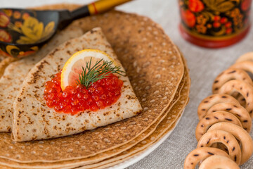 Russian traditions. Russian holiday Maslenitsa. Still life with a stack of pancakes, red caviar, lemon and wooden spoons (Khokhloma).