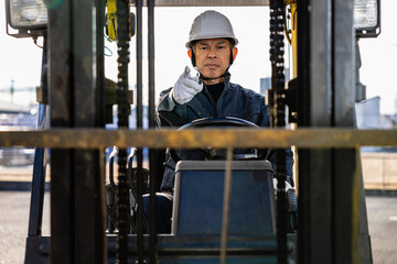 Fototapeta na wymiar Middle-aged Asian male worker with forklift on factory grounds.