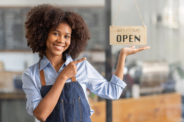 Successful african woman in apron standing coffee shop door. Happy small business owner holding...