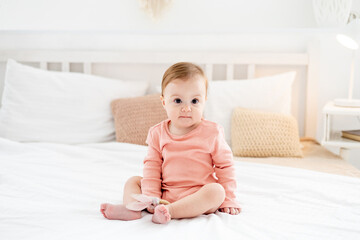 a baby girl on a bed in a bright bedroom in a pink bodysuit smiling or laughing