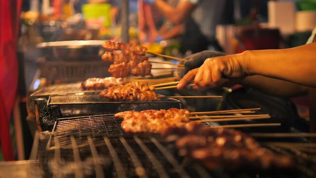 Local Asian Street Food. Chef Cooking Chicken Satay on Fire Bbq Grill at Night Market in Phuket Old Town. High Quality Cinematic 4K Slowmotion Thai Cuisine Footage. Thailand.
