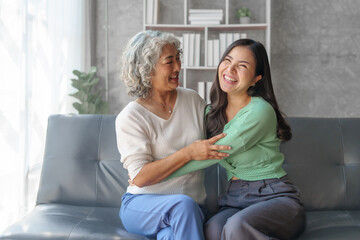 60s asian mother elderly sitting on sofa with young asia female daughter together in living room....
