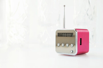Cute little modern radio with antenna on a white background. New pink cube radio receiver with copy space. Wireless hi-tech electronic mass media equipment