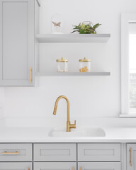 Fototapeta na wymiar A gold faucet detail with grey cabinets, white marble countertop, and decorations on shelves.