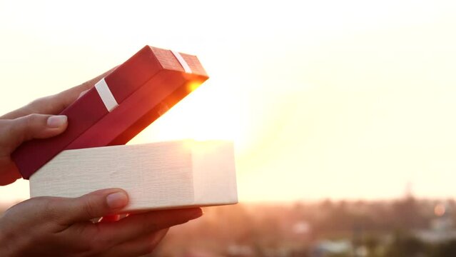happy woman opening gift box with white ribbon, surprise present over sunset or sunlight in natural outdoor background. Concept of valentine day, giftbox, present, gift, Xmas, Christmas, 4K
