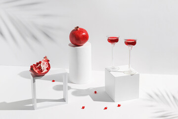 Two glasses of red juice or wine and pomegranates on a geometric podiums on white background with shadow. Summer refreshment concept. Minimal style.