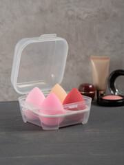Many multi-colored beauty blenders in plastic box on grey table. Professional makeup tools. Background for beauty blogger