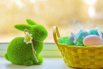 green grass rabbit and basket with colorful eggs on windowsill. Easter symbol, decor, bunny figure