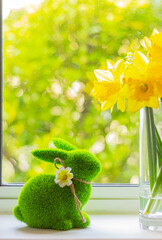 Easter symbol, decor, bunny figurine and daffodils. green grass rabbit and yellow flowers in vase on windowsill