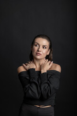 Fototapeta premium Fashion concept. Sexy looking woman with dark clothes and wet hair style studio portrait in black background. Grace pose and seductive look of the model away the camera. Hands placed on shoulders