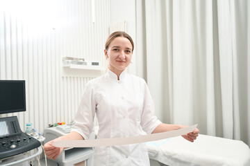 Female doctor is standing in her office with result of heartbeat of patient