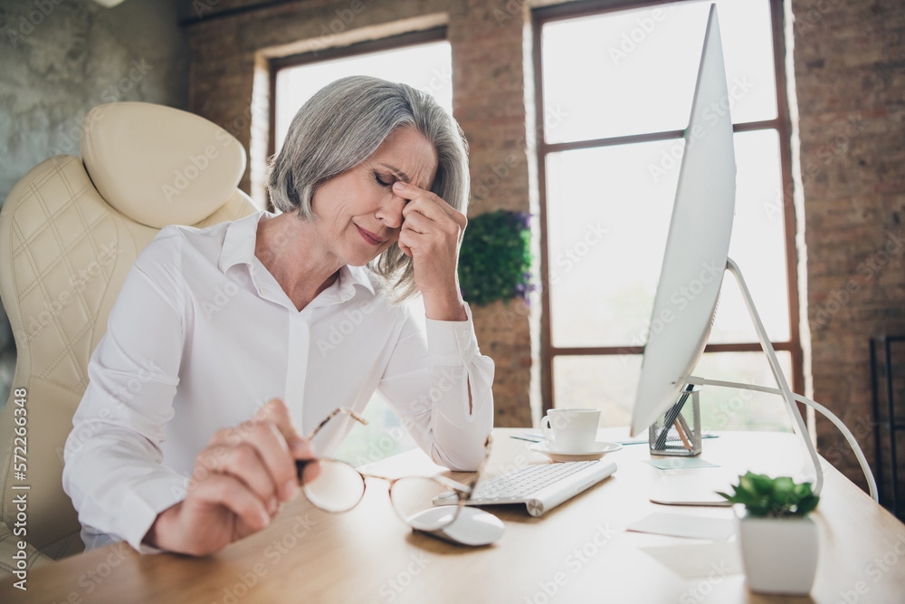 Sticker Profile portrait of sad unsatisfied exhausted aged lady sitting chair hand fingers touch nose suffer headache workstation indoors