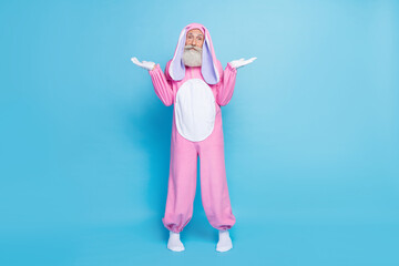 Full size photo of uncertain elderly pensioner wear pink bunny costume shrugging shoulders have no idea isolated on blue color background - obrazy, fototapety, plakaty