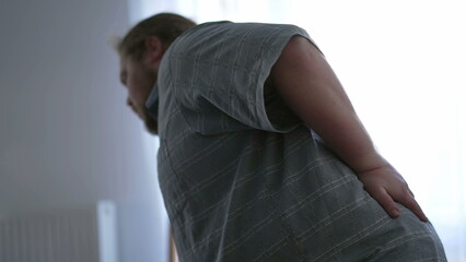 One overweight man having back pain by getting up from couch. A sedentary fat male person having...