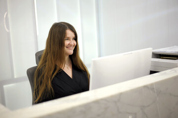 A young woman sits at a computer at the reception of a white light office hospital dentistry any...