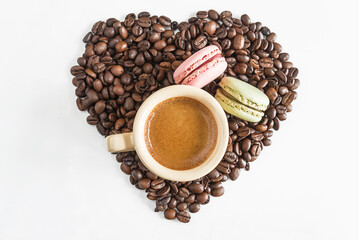 heart of coffee beans with cup of coffee and two macarons on white background