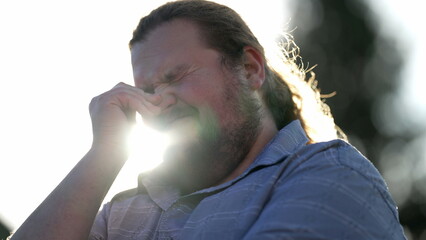 Frustrated young man feeling anxiety and worry standing outdoors in sunlight. Pensive preoccupied emotion of a chubby man feeling regret
