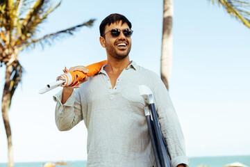 Man carrying beach umbrella and beach chair during his tropical beach vacation.